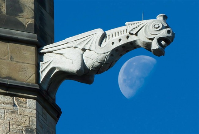 The moon is seen past a gargoyle on the Peace Tower of Parliament Hill in Ottawa on October 25, 2013.
