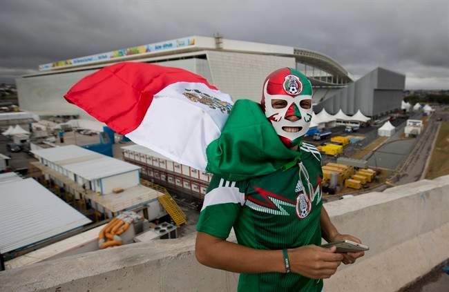 Backdropped by the Itaquerao stadium, a Mexico soccer fan poses for a photo wearing a wrestling mask and a representation of his country's national flag as a cape, in Sao Paulo, Brazil, Tuesday, June 10, 2014.