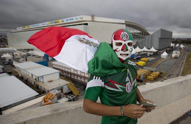 Backdropped by the Itaquerao stadium, a Mexico soccer fan poses for a photo wearing a wrestling mask and a representation of his country's national flag as a cape, in Sao Paulo, Brazil, Tuesday, June 10, 2014.
