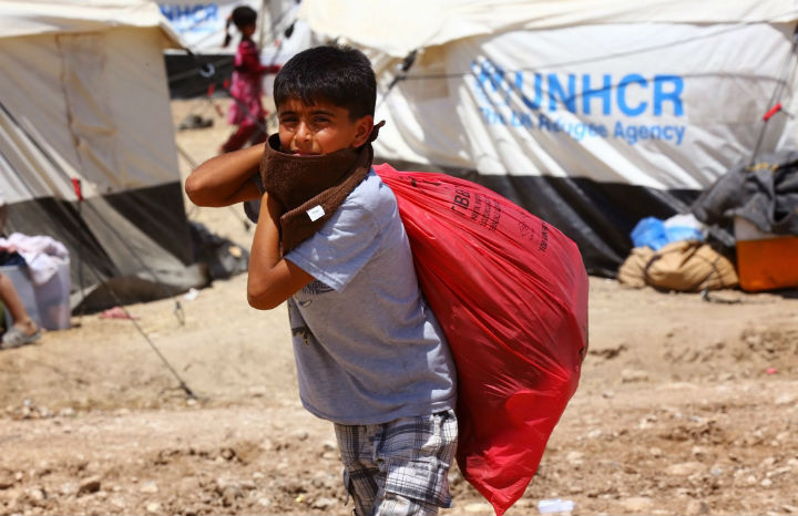 An Iraqi boy who fled fighting between security forces and al-Qaida inspired militants in his hometown of Tal Afar carries his belongings at Germawa camp for displaced Iraqis, in a hot dusty plain in the largely-autonomous Kurdish area of Dahuk, 430 kilometers northwest of Baghdad Tuesday, June 17, 2014.