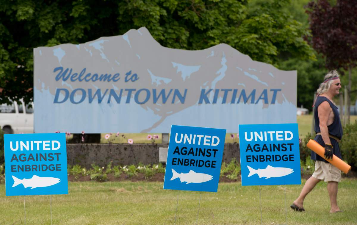 A man walks by signs opposing the Enbridge pipeline in downtown Kitimat, B.C. Tuesday, June, 17, 2014. 