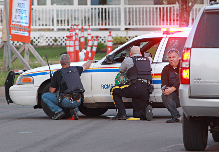Police officers take cover behind their vehicles in Moncton, New Brunswick, on Wednesday June 4, 2014.