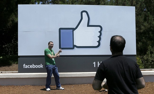 In this June 11, 2014 photo, a man poses for photographs in front of the Facebook sign on the Facebook campus in Menlo Park, Calif.
