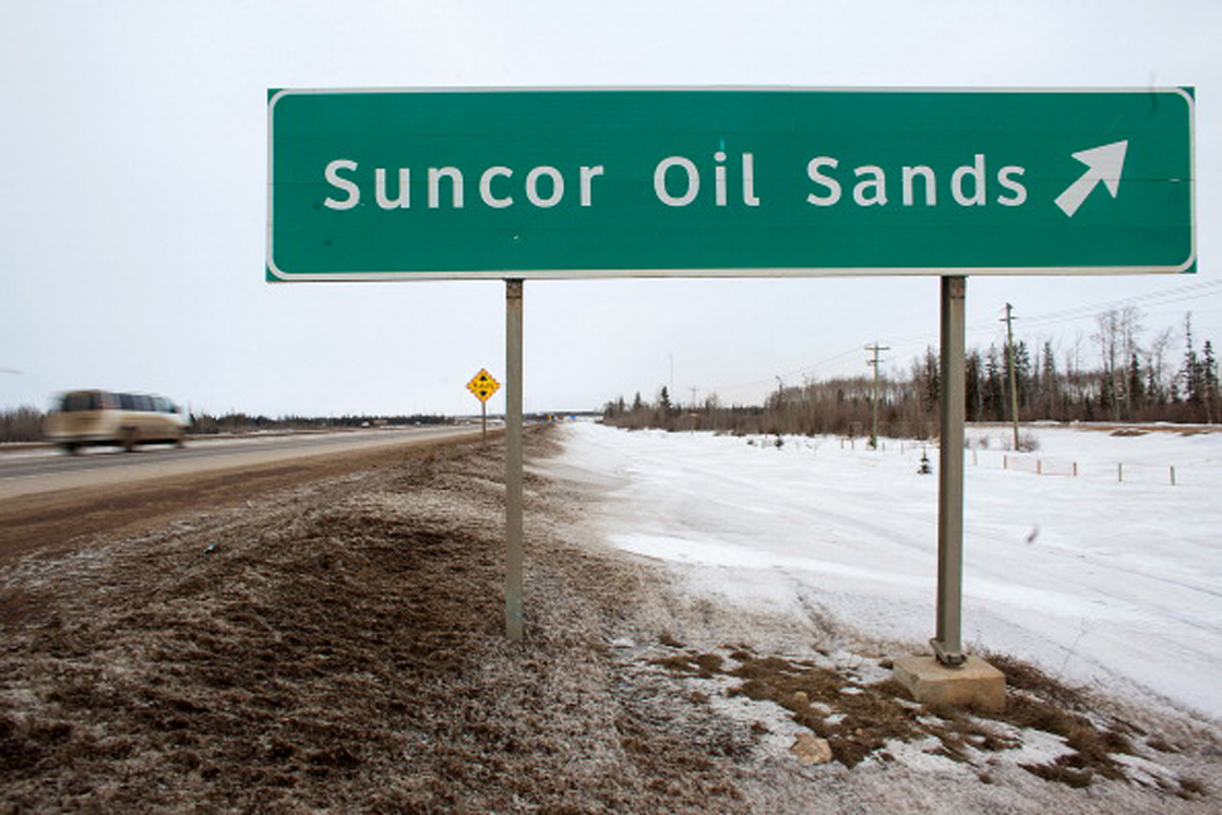 A sign directing traffic to the Suncor Energy Inc. base plant stands at the Athabasca Oil Sands near Fort McMurray, Alberta, Canada, on Tuesday, March 26, 2013. Canadian light oil prices retreated from a six-month high on the spot market reached last week as production slipped and refineries prepared for maintenance. Photographer: Brett Gundlock/Bloomberg via Getty Images