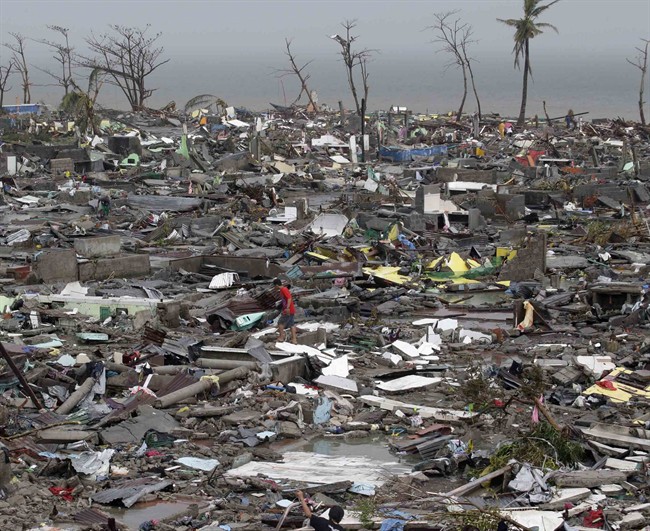 In this Nov. 10, 2013 file photo, a man walks through debris of houses destroyed by Typhoon Haiyan in Tacloban city, Leyte province, central Philippines.