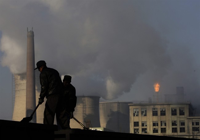 FILE - In this Nov. 30, 2007 file photo, backdrop by cooling towers of a power plant and chemical factory, miners shovel coal at a mine in Xiahuayuan county, north China's Hebei province.