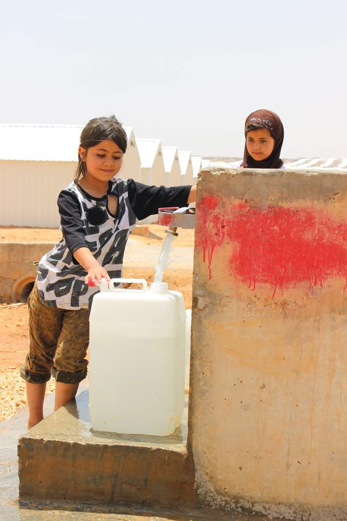 Girls fill a water jug in Azraq Camp in Jordan