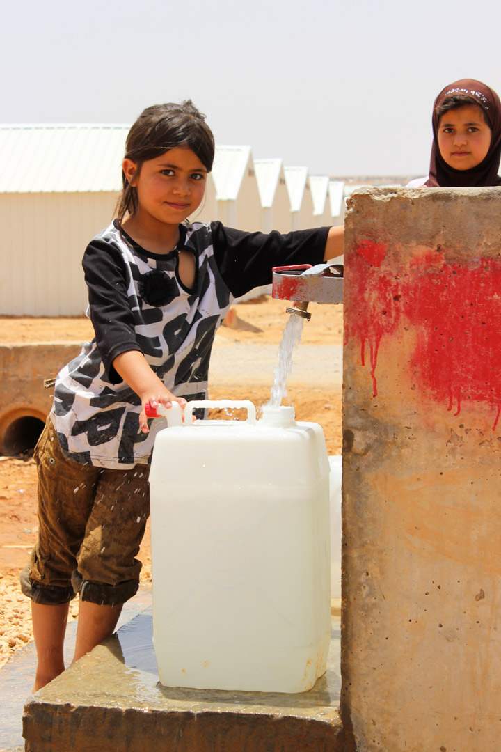 Girls fill a water jug from a tap in Azraq Camp