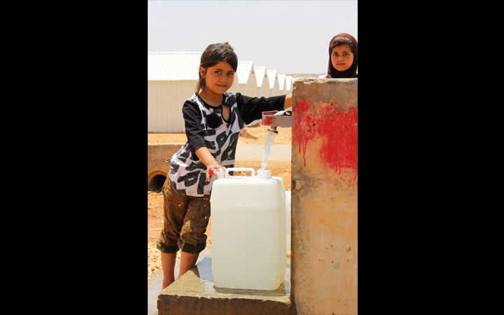 Girls fill a water jug in Azraq Camp