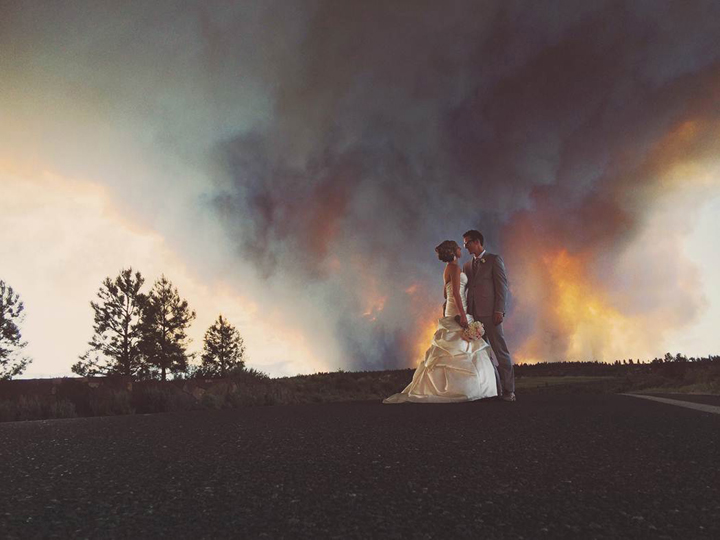 In this Saturday, June 7, 2014 photo provided by Josh Newton, newlyweds Michael Wolber and April Hartley pose for a picture near Bend, Ore., as a wildfire burns in the background. Their ceremony had to be evacuated and their reception was relocated because of the fire.