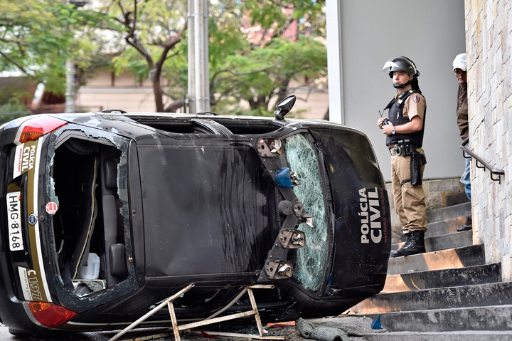 A police officer stands next to a destroyed police car during a violent demonstration at the 2014 soccer World Cup in the center of Belo Horizonte , Brazil, Thursday, June 12, 2014.