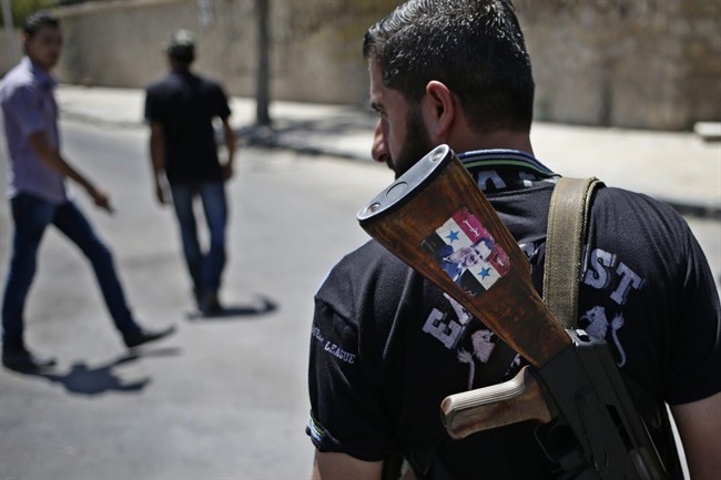 This Aug. 21, 2013 file photo shows a Syrian military soldier holding his AK-47 with a sticker of Syrian President Bashar Assad and Arabic that reads, "Syria is fine," as he stands guard at a check point in Damascus, Syria. 