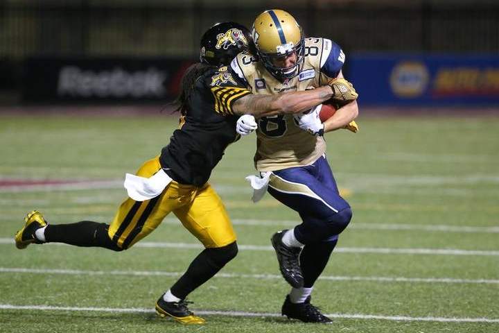 Rico Murray #0 of the Hamilton Tiger-Cats forces a fumble during CFL game action as Julian Feoli-Gudino #83 of the Winnipeg Blue Bombers is stripped off the ball on Thursday at Ron Joyce Stadium in Hamilton, Ont.