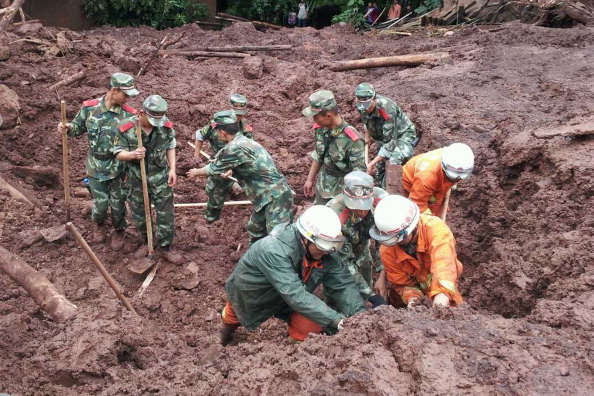 Rescuers search for buried people at the site of a mudslide at Longtoushan Town on July 7, 2014 in Ludian County, Yunnan Province of China. At least four people were killed and seven others remained missing after rainstorm-triggered mudslides hit Ludian County on Sunday.  (Photo by ChinaFotoPress/Getty Images).