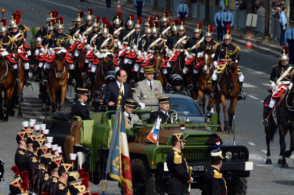 French President Francois Hollande (C) and French Army Chief of Staff, General Pierre de Villiers (R), escorted by Republican Guards on horseback, arrive on Concorde square aboard their command car after reviewing troops down the Champs-Elysees avenue during the annual Bastille Day military parade in Paris, on July 14, 2014.  