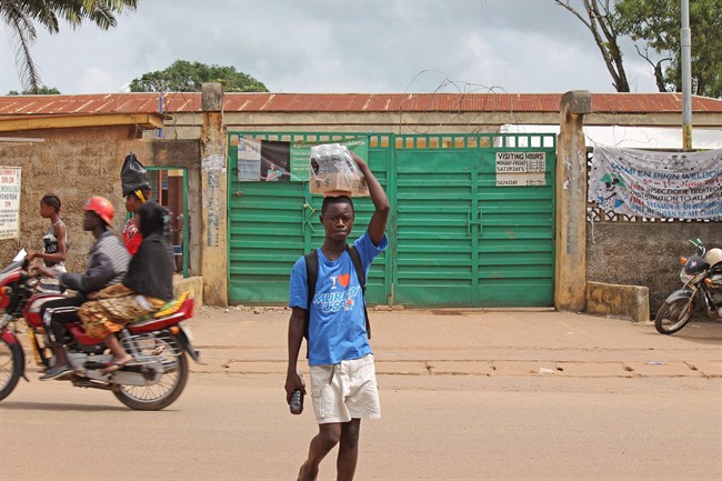 In this photo taken on Sunday, July 27, 2014, a boy, centre, selling soft drinks walk past a clinic taking care of Ebola patients in the Kenema District on the outskirts of Kenema, Sierra Leone.
