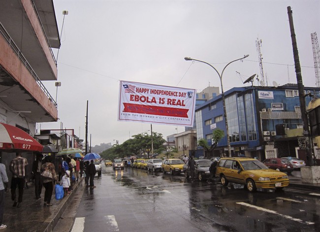 In this photo taken on Monday, July 28, 2014, people hang out in a street under a banner which warns people to be cautious about Ebola, in Monrovia, Liberia. 