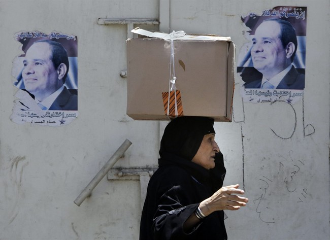 An elderly Egyptian vendor walks past old election posters supporting newly elected President Abdel-Fattah el-Sissi in Cairo, Egypt, Saturday, July 5, 2014.