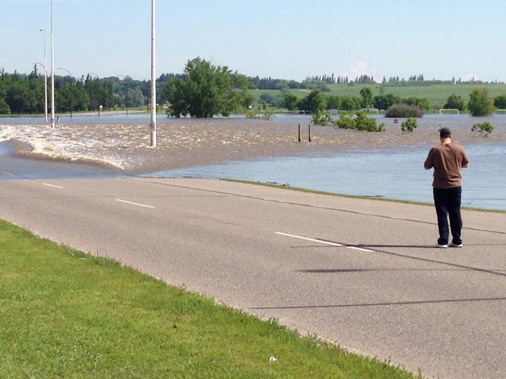 A resident watches Assiniboine River floodwaters wash over First Street in Brandon, Man.