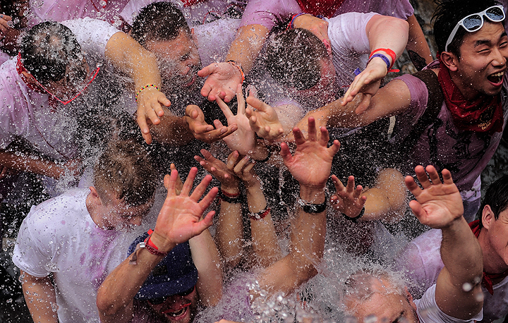 Revelers enjoy water being thrown from a balcony during the launch of the ‘Chupinazo’ rocket, to celebrate the official opening of the 2014 San Fermin fiestas, in Pamplona, Spain, Sunday, July 6, 2014.