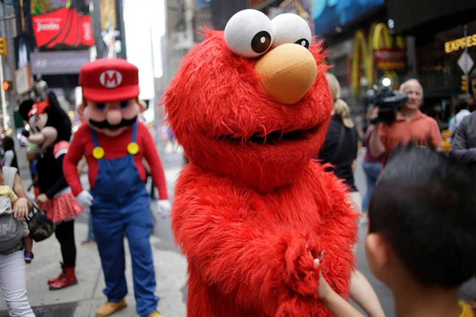 A person dressed as Elmo shakes hands with a pedestrian in Times Square. Mayor Bill de Blasio said Monday that he believes the people wearing character costumes in Times Square should be licensed and regulated.  (AP Photo/Seth Wenig).