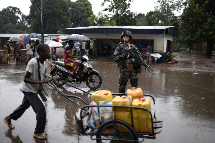 A French soldier of the Sangaris force patrols as a man pushes a trolley with plastic cans on July 8, 2014 through the PK12 area of Bangui, Central African Republic.