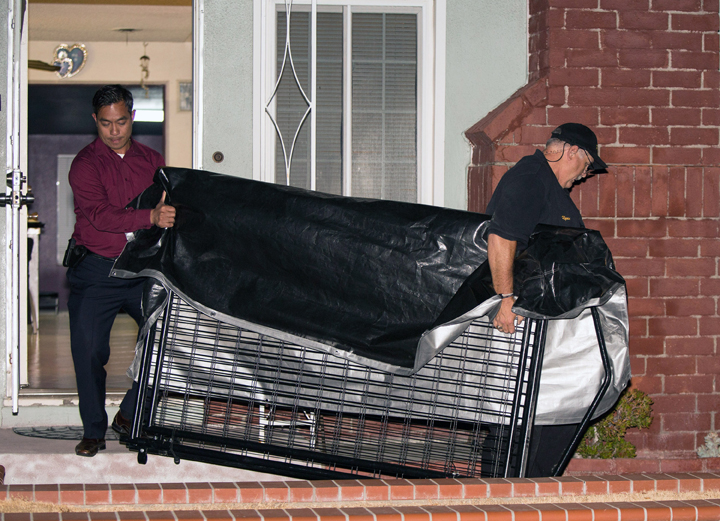 In this Tuesday, July 1, 2014 photo, a crime scene investigator and a detective carry a cage from a residence in Anaheim, Calif. 
