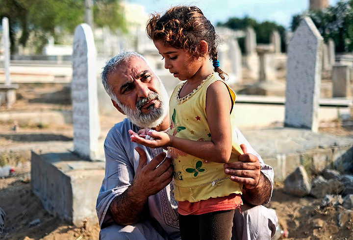 A relative guides a girl in prayer at the grave of their loved one in a cemetery in Gaza city, northern Gaza Strip, Monday, July 28, 2014. Monday marked the beginning of the three-day Eid al-Fitr holiday, which caps the Muslim fasting month of Ramadan.