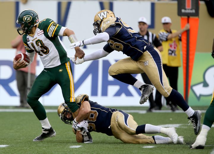 Edmonton Eskimos' quarterback Mike Reilly (13) tries to break away from Winnipeg Blue Bombers' Jason Vega (98) and Ian Wild (38) during first half CFL Football at Investors Group Field in Winnipeg, Manitoba, Canada.