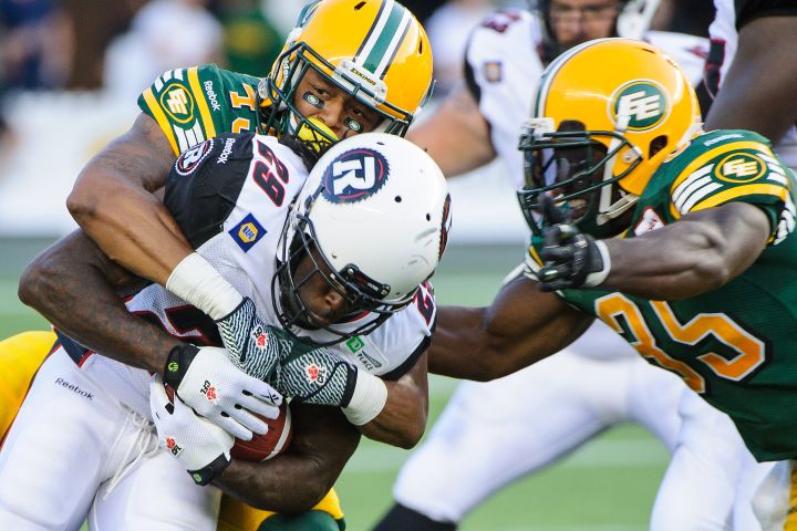 Dexter McCoil #45 (L) and Rennie Curran #35 (R) of the Edmonton Eskimos stop Chevon Walker #29 of the Ottawa Redblacks during a CFL game at Commonwealth Stadium on July 11, 2014 in Edmonton, Alberta, Canada.