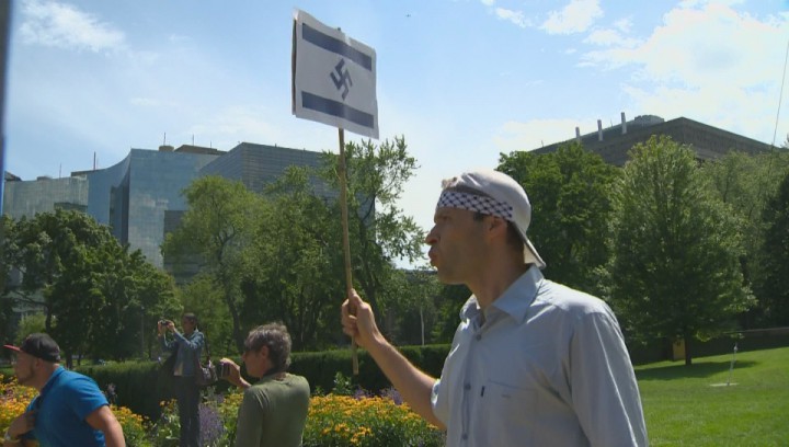 Protester holding a sign of the Israeli flag with a swastika instead of the Star of David. (Global News)