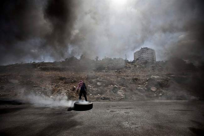 A Palestinian man burns a tire during clashes with Israeli soldiers following a protest against the Israeli offensive in Gaza, outside Ofer, an Israeli military prison near the West Bank city of Ramallah, Friday, July 18, 2014. Israeli troops pushed deeper into Gaza on Friday to destroy rocket launching sites and tunnels.
