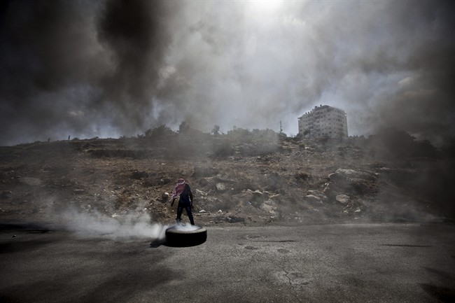 A Palestinian man burns a tire during clashes with Israeli soldiers following a protest against the Israeli offensive in Gaza, outside Ofer, an Israeli military prison near the West Bank city of Ramallah, Friday, July 18, 2014.