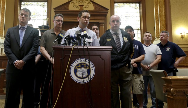 Jersey City Mayor Steven Fulop, centre, addresses the media during a news conference talking about an early morning shooting which led to a suspect and a Jersey City Police Department officer killed, Sunday, July 13, 2014, in Jersey City, N.J. 