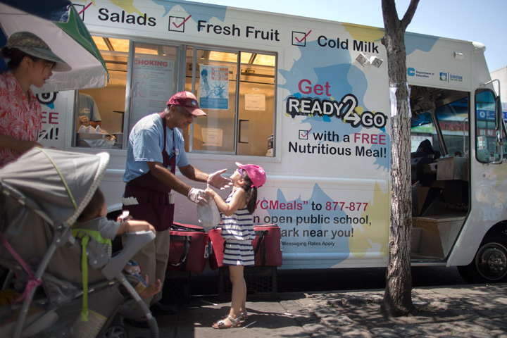 In this July 23, 2014 photo, young adults and small children accompanied by parents receive free lunches at the Get Ready 2 Go truck in the Flushing neighborhood of the Queens borough of New York. The city’s Department of Education has turned to food trucks as part of its summer meals program. The program tries to make sure the children who qualify for reduced-price or free meals during the academic year don’t lose out just because school’s closed.