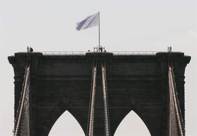 New York City Police officers stand at the base of a white flag flying atop the west tower of New York's Brooklyn Bridge, Tuesday, July 22, 2014.
