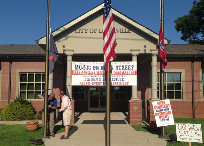 Lobelville Mayor Robby J. Moore, right, and business owner Robert Mathis lower flags in front of City Hall in Lobelville, Tenn., Thursday, July 10, 2014.