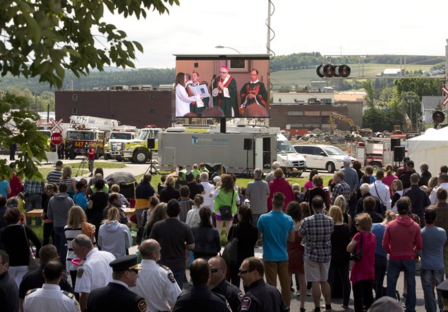 People watch the mass outside the church on a screen overlooking downtown Sunday, July 6, 2014 in Lac-Megantic, Que.
