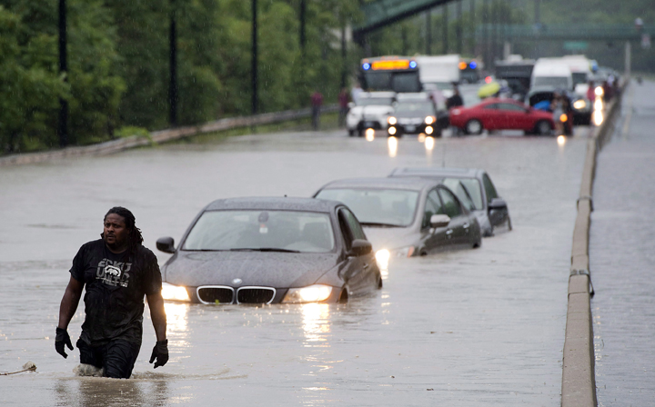 A tow truck driver walks back through flood waters after hooking up a car on the Don Valley Parkway in Toronto on Monday July 8 2013.
