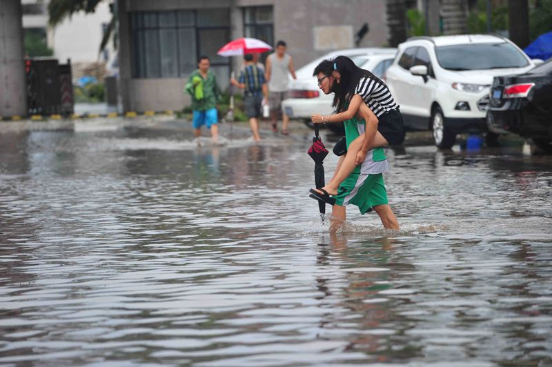 A man carrying a woman walks in a flooded street on July 19, 2014 in Haikou, Hainan Province of China. (Photo by ChinaFotoPress/ChinaFotoPress via Getty Images).
