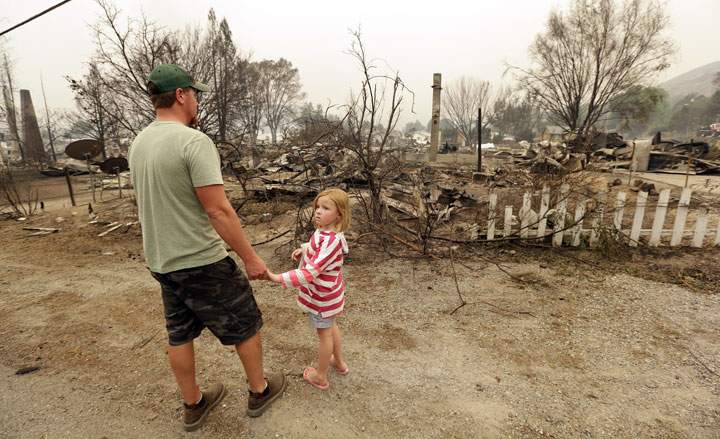Forrest Harrison holds the hand of his daughter, Avery, 5, as he looks over the rubble remaining from his home after a wildfire destroyed it the night before Friday, July 18, 2014, in Pateros, Wash.