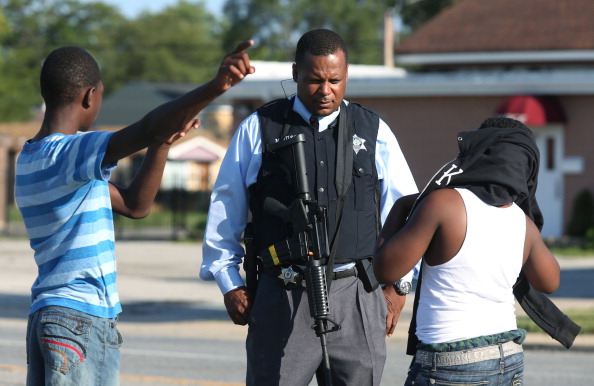 A police officer talks with young residents at 147th Street and South Hoyne Avenue, two blocks from an on-going hostage situation on Tuesday, Aug. 19, 2014, in Harvey, Ill. Two officers were shot during the incident. (John J. Kim/Chicago Tribune/MCT via Getty Images).