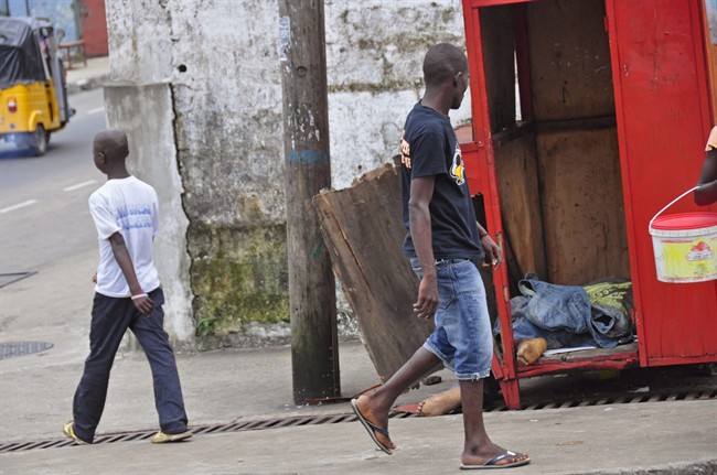 In this photo taken on Saturday, Aug. 16, 2014, a man looks at the body of another man suspected of dying from the Ebola virus on one of the busiest streets in Monrovia, Liberia. 