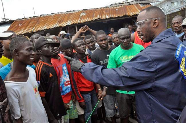 A Liberian policeman warns residents of the West Point area to be calm, as they wait for a second consignment of food from the Liberian Government to be handed out, at the West Point area, near the central city area of Monrovia, Liberia, Friday, Aug. 22, 2014. 