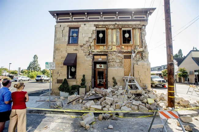 Pedestrians stop to examine a crumbling facade at the Vintner's Collective tasting room in Napa, Calif., following an earthquake Sunday, Aug. 24, 2014.