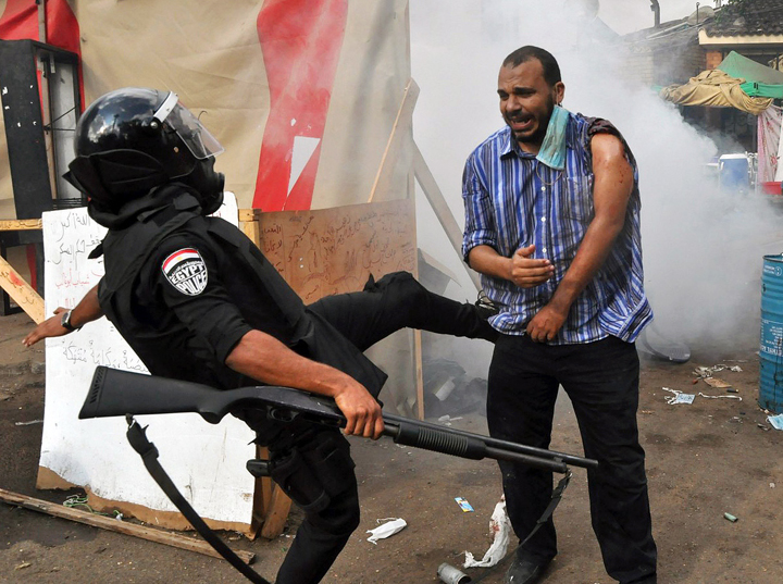  In this Wednesday, Aug. 14, 2013 file photo, an Egyptian policeman kicks a supporter of ousted Islamist President Mohammed Morsi as they clear a sit-in camp set up near Cairo University in Cairo's Giza district, Egypt. 