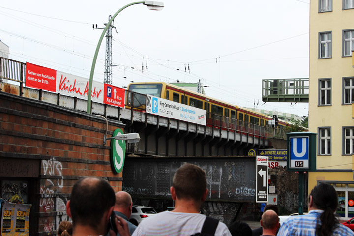 An elevated S-Bahn train glides above a busy street in East Berlin.