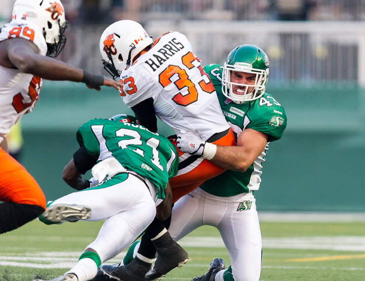 Andrew Harris #33 of the BC Lions fights off a tackle from Terrell Maze #20 and Brian Peters #27 of the Saskatchewan Roughriders in a game between the BC Lions and Saskatchewan Roughriders in week 3 of the 2014 CFL season at Mosaic Stadium on July 12, 2014 in Regina, Saskatchewan, Canada.