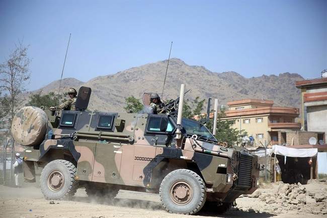 A NATO soldier, right, opens fire in an apparent warning shot in the vicinity of journalists near the main gate of Camp Qargha, west of capital Kabul, Afghanistan, Tuesday, Aug. 5, 2014. 