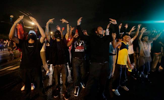 People defy a curfew Sunday, Aug. 17, 2014, before smoke and tear gas was fired to disperse a crowd protesting the shooting of teenager Michael Brown last Saturday in Ferguson, Mo. Brown\’s shooting in the middle of a street following a suspected robbery of a box of cigars from a nearby market has sparked a week of protests, riots and looting in the St. Louis suburb.